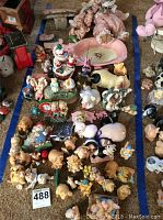 Wide view of many pig and farm animal figurines arranged on carpet, showing variety of designs and colors.