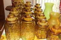 Photo showing multiple yellow glass jars with lids arranged in rows showing embossed pattern and color.