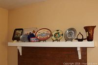 View of all decorative plates and hand blown vase arranged on a mantle.