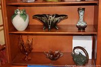 Shelf display showing white ceramic frog bowl, dark glass vase, and small patterned glass vase.