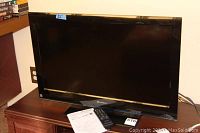 Front view of the 32-inch black Sansui LED TV on a wooden cabinet with remote and manuals laid out in front.