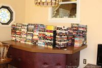 Photo of a large number of VHS tapes stacked on a counter, showing the volume and variety in the lot.