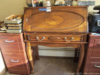 Full view of the wooden secretary desk with drop-front panel closed, showing oval inlaid pattern on the front and cabriole legs.