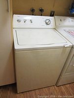 Full view of white Whirlpool top-loading washing machine positioned next to a dryer, showing standard design with lid closed.