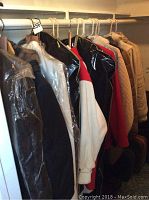 Photo showing multiple ladies outerwear jackets and coats on hangers, covered in plastic for protection, colors include black, white, red, tan, and patterned.