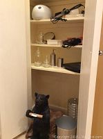 Shelf with clear and frosted glass bathroom containers, stainless soap dispenser, black Revlon curling iron, and black corded device.
