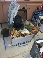 Wide view of the lot showing white folding chairs, box with assorted items including baskets, faux flowers, decorative plate, and a black bag.