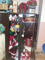 Full view of Christmas decor stored inside a cabinet, showing animated Santa, Santa plushes, baskets, and other decorations
