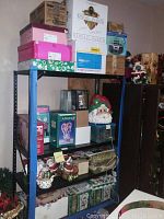 Shelf with boxes and Christmas-themed ceramic decor including Santa cookie jar, candle holders, various ceramic pieces, and boxed dinnerware sets.