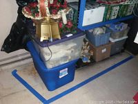 Wide shot of stacked plastic bins with holiday decor including wreath, lamp, and boxed items on shelving