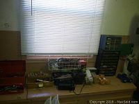 Image of wooden shelf with baskets containing assorted small tools, hardware, and miscellaneous items under a window with blinds.