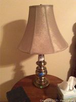 Full view of brass table lamp with beige bell-shaped lampshade on wooden surface