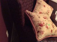 Wing back chair with floral pillows visible on seat and backrest, dark upholstery.