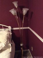 Full view of the 5-light floor lamp in a corner beside a bed, with curved metal arms and frosted glass shades.