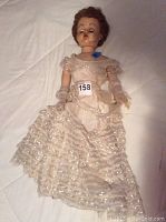 Full body photo of the vintage 28-inch doll in a torn lace dress lying on a white surface, showing wear and tear on clothing and doll body.