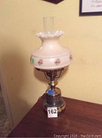 Full view of Victorian style table lamp with cream glass floral shade and brass metal base on wooden surface.