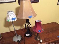 Photo showing all three lamps together on a wooden surface, including the maroon shade lamp, painted shade lamp, and beige shade lamp on black base.