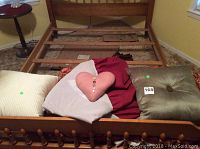 Photo showing various throw pillows including white with stripes, pink heart-shaped, green with button center, dark red comforter, and wooden bed frame