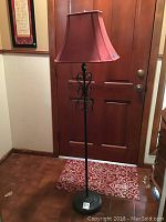 Full view of the metal floor lamp with red fabric shade standing on a tile floor near a door.