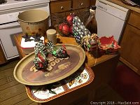 Photo of wire rooster basket containing artificial fruit and surrounding decorative items including tins, ceramic roosters, salt and pepper shakers, and small dishes.