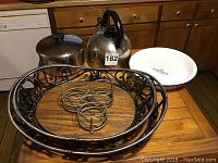 Photo showing Revere Ware 2 quart pot missing handle, metal teapot, and two metal and wood serving trays on a wooden table.