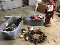 Photo showing standing cloth Santa figure, two plastic bins with garlands and greenery, and wreath lying on floor