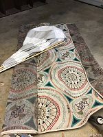 Outdoor area rug rolled and partially unrolled on floor with white wooden poles and cloth leaning on it.