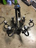 Full view of black metal chandelier light fixture with curled arm design and eight bulb sockets on concrete floor.