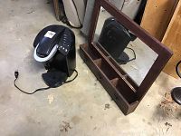 Photo showing Keurig coffee maker and wooden mirror decor side by side on floor.