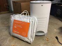 Dekor diaper pail closed next to packaged queen microfiber comforter