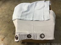 Pottery Barn curtain panel folded showing bronze-colored grommets on beige fabric.