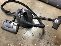 Fuller vacuum cleaner with hose and two floor attachments laid on a concrete floor showing overall condition.