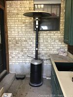 Full view of the 7 feet tall black outdoor propane heater standing beside a brick wall and kitchen cabinetry.