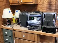 Overview of Aiwa stereo system with two speakers, GE alarm clock radio, two lamps on wooden counter.