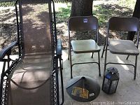 Three outdoor chairs including one reclining lounge chair and two folding metal chairs along with a metal squirrel baffle and the decorative lantern shown on concrete patio.