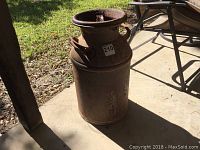 Full view of rusted milk can showing overall unknown height and cylindrical shape with handles on sides.