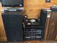 Two black Fisher speakers with fabric grille covers and visible driver shapes inside, placed near audio equipment rack.