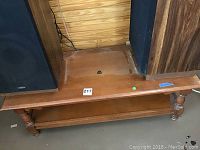 Wood coffee table showing top surface, two turned legs, and underside shelf, with visible scratches and wear marks.
