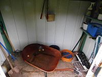 Wheelbarrow, assorted gardening tools including a bucket, placed against shed wall