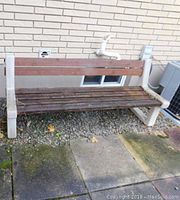 Full view of the bench against a brick wall, showing white plastic bench ends and dark brown wooden slats for seat and backrest.