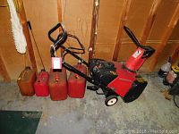 Full view of red Honda snow blower with five plastic gas cans lined up