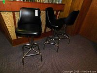 Three black vinyl and metal swivel bar stools positioned side by side. One stool displays vinyl damage on the seat.