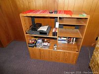 Wide shot of shelving unit featuring the VHS player, tape rewinder, VHS tapes, CDs, CD wallet, and lens cleaner.