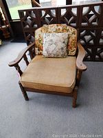 Front view of wood frame arm chair with beige upholstered seat and floral back cushion with floral accent pillow.