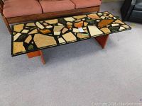 Side view of the coffee table showing the stone fragment epoxy resin top and wood base with wear and scrapes.