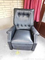 Front view of black vinyl recliner chair showing tufted backrest and padded arms.