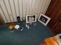 Overview photo showing all items laid on carpet in front of wallpapered wall and wood panel, including vases, birds, coasters, dog photos.