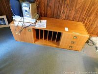 Front view of entertainment unit showing cabinet door, vertical slots, and three drawers with brass handles.