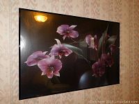 Framed floral print showing pink flowers and green leaves on a dark background with some light reflections.