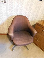Front view of fabric swivel chair with brown textured upholstery next to wooden furniture, showing general shape and condition.